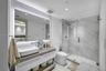 Floating vanity with a rectangular vessel sink and wood-finish countertop, full-height backlit mirror, walk-in glass shower enclosure with stone-finis