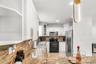 Kitchen featuring white cabinetry with gold-tone hardware, stone countertops, stainless steel appliances, and contemporary pendant lighting