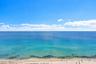 Panoramic oceanfront perspective featuring clear blue waters, expansive horizon, and sandy shoreline