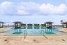 Expansive swimming pool featuring built-in cabanas, stone-paver decking, and stainless steel handrails