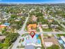 Aerial view of corner lot property featuring a light-toned multi-gabled roof, an expansive paved driveway, a private in-ground pool, and mature perime