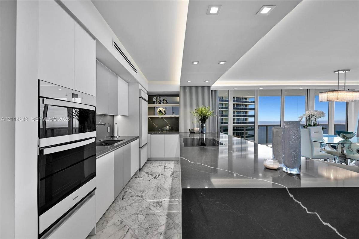 Kitchen featuring high-gloss cabinetry, stone-finish countertops, integrated double wall ovens, recessed ceiling lighting, and floor-to-ceiling window