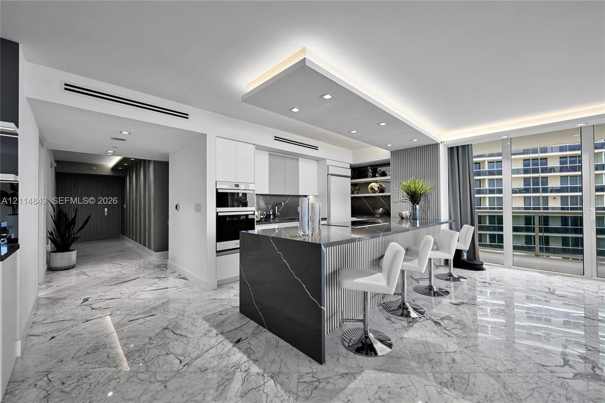 Kitchen featuring a central island with a stone countertop and waterfall edge, flat-panel cabinetry, a built-in wall oven, recessed ceiling lighting, 