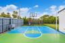 Outdoor area featuring a painted hard-surface court, a built-in basketball hoop, a dedicated putting green, and enclosed by wood-panel fencing