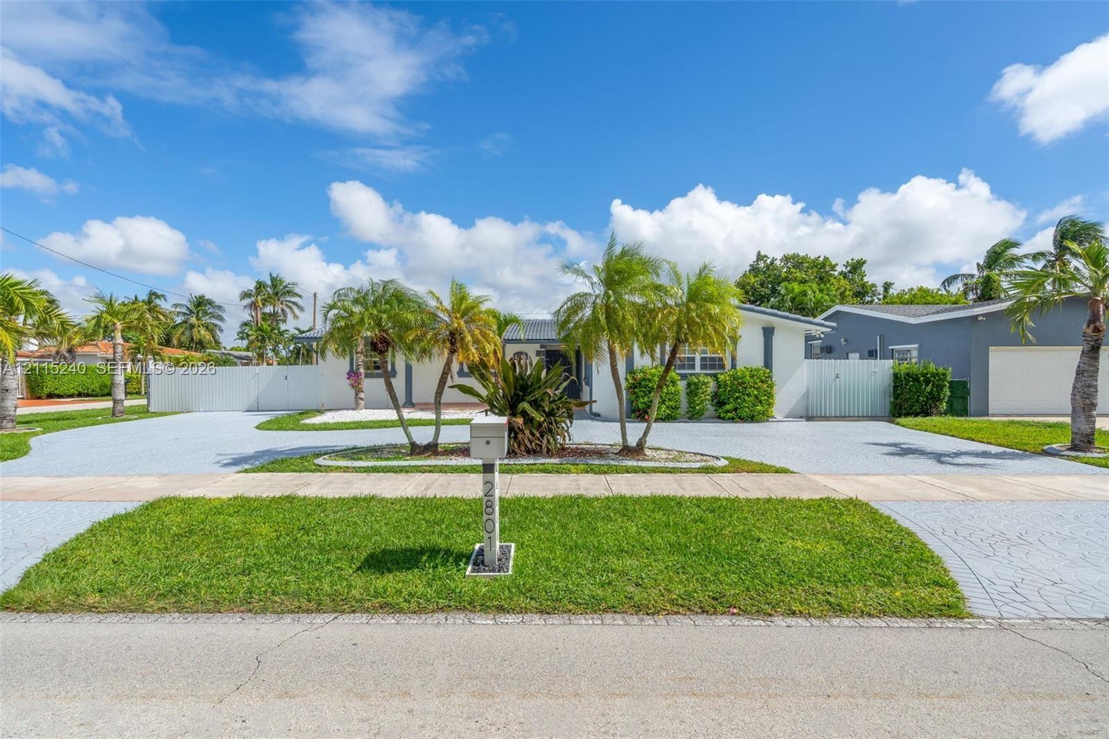 Single-story exterior featuring a stamped concrete driveway, lush palm tree landscaping, and perimeter privacy fencing