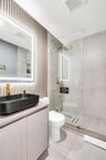 Bathroom featuring a slate-toned vessel sink, gold-tone hardware, a wall-mounted LED-backlit mirror, vertical slat accent wall, and a glass-enclosed w