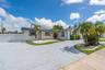 Single-story exterior featuring a decorative paved driveway, white stucco finish, dark shingle roof, integrated landscaping beds, and a white privacy 