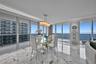Floor-to-ceiling glass walls, polished stone flooring, recessed ceiling lighting, and a multi-light pendant fixture