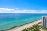 Panoramic ocean exposure featuring a sandy coastline, shoreline vegetation, and proximity to high-rise structures