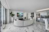 Open-concept living space featuring white stone-finish flooring, recessed lighting, built-in electric fireplace, recessed wet bar with shelving, and k