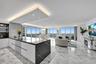 Open-concept living space featuring stone flooring, floor-to-ceiling windows, a center kitchen island with a dark stone waterfall countertop, recessed