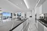 Modern kitchen featuring a large central island with veined stone countertop and integrated cooktop, handle-less cabinetry, built-in double ovens, and