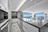 Contemporary kitchen featuring custom flat-panel cabinetry, a large waterfall-edge island with solid surface countertop, built-in appliances, recessed