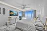 Floor-to-ceiling windows, light-toned stone-finish flooring, recessed LED cove lighting, modern ceiling fan, and built-in wall-mounted cabinetry