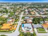 Aerial perspective of a corner lot property featuring a multi-pitched roof, an expansive paved driveway, a gated swimming pool, and a dedicated athlet
