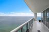 Covered balcony featuring oversized tile flooring, a glass panel railing, and expansive ocean scenery