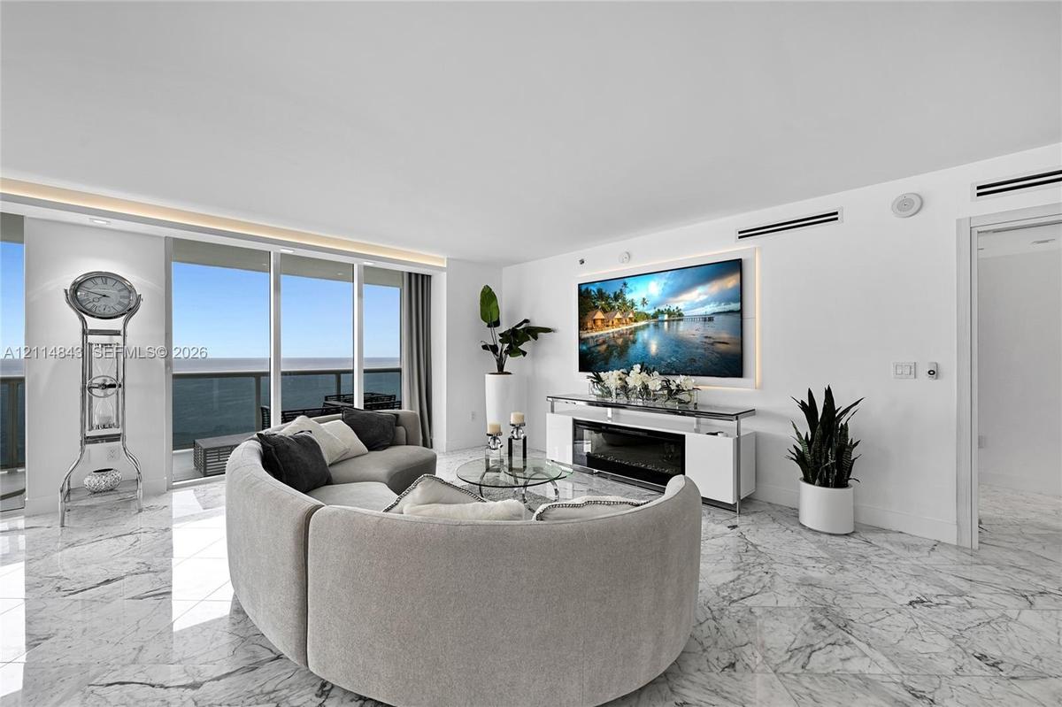Open-concept living space featuring floor-to-ceiling glass windows, polished stone flooring, recessed ceiling accent lighting, and a built-in electric