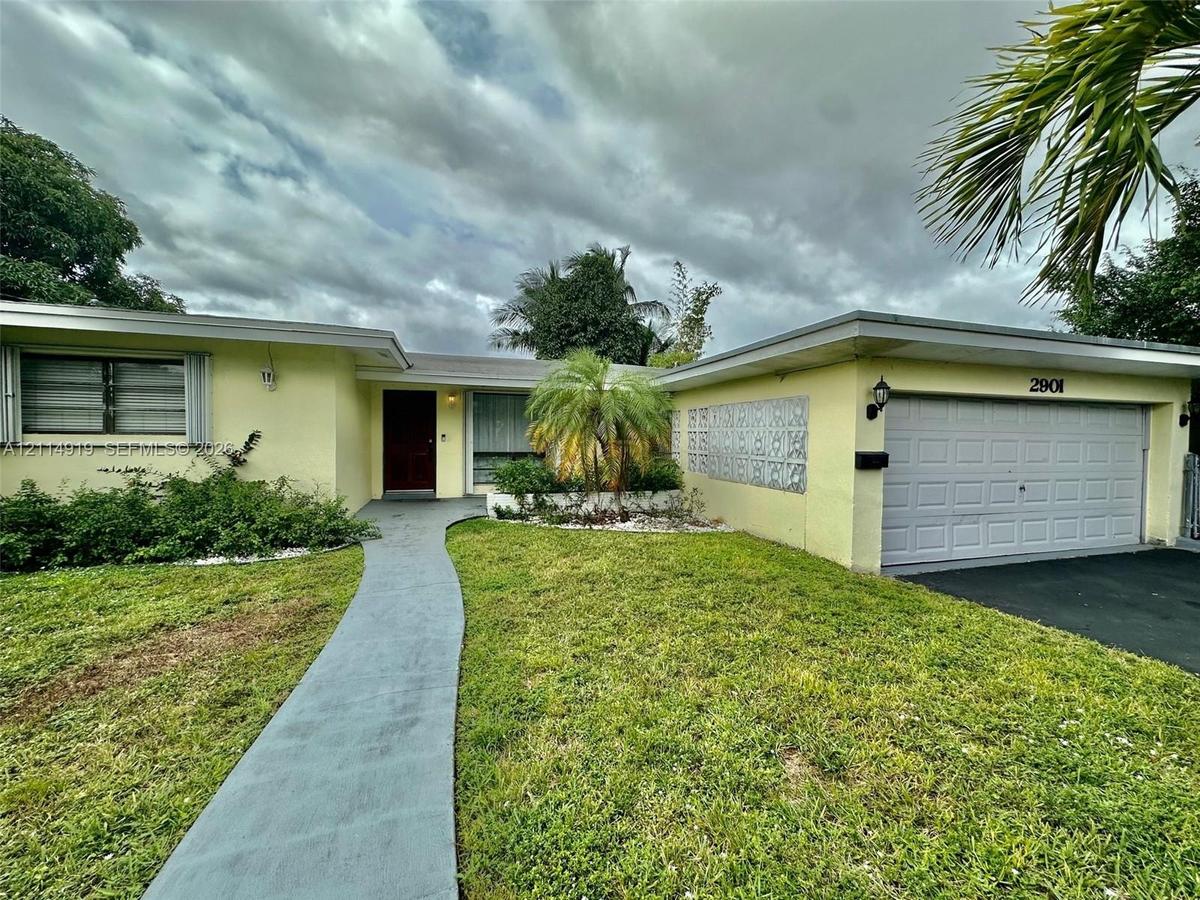 Single-story residence featuring a concrete walkway, attached two-car garage, decorative exterior masonry screen, and mature landscape plantings