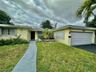 Single-story residence featuring a concrete walkway, attached two-car garage, decorative exterior masonry screen, and mature landscape plantings