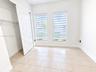 Neutral-toned ceramic tile flooring, dual windows with installed roller shades, and a closet featuring a multi-panel door and wire shelving