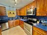 Kitchen featuring wood cabinetry, stainless steel appliances, blue solid-surface countertops, blue mosaic tile backsplash, and dual-basin stainless st
