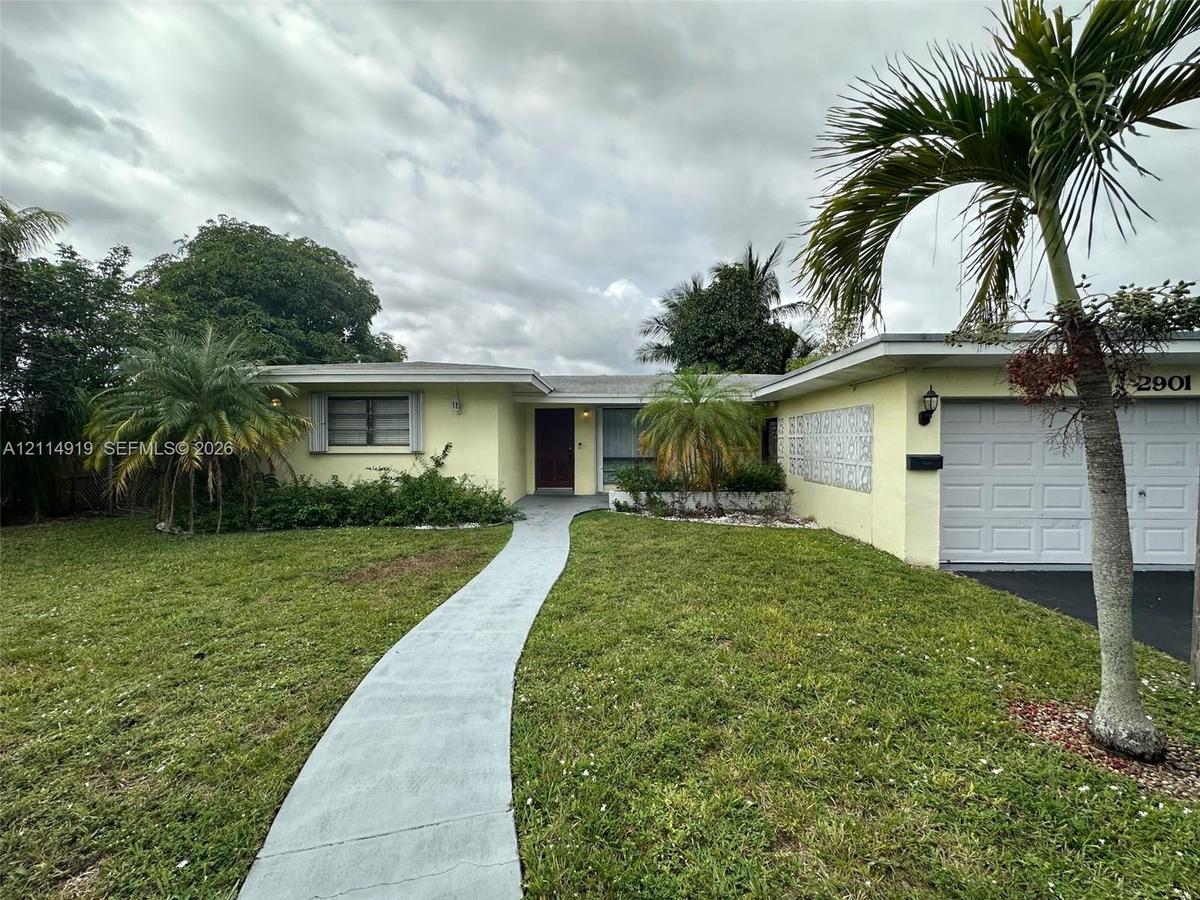 Single-story residence featuring a painted stucco exterior, decorative breeze block wall detailing, an attached garage, and a concrete walkway
