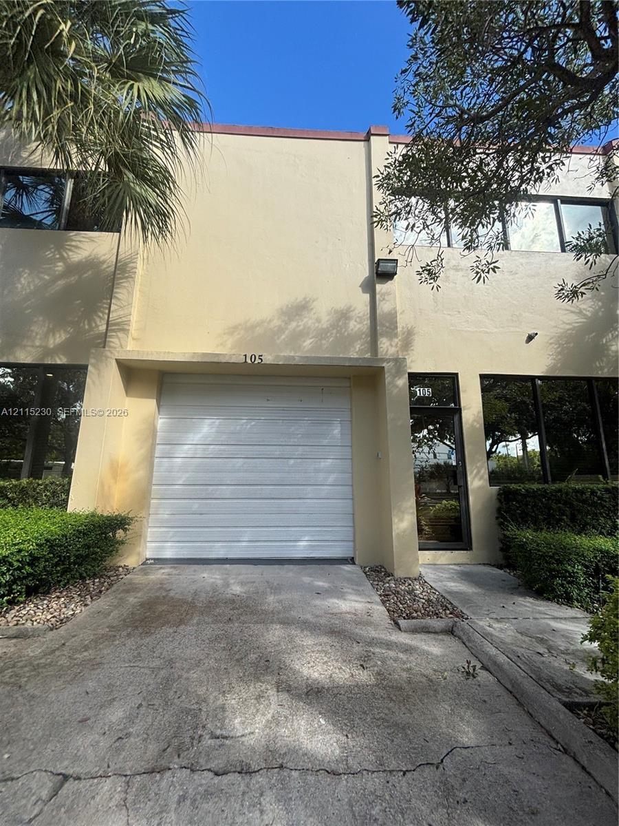 Two-story exterior featuring a stucco facade, single-car garage with a roll-up door, glass-paneled entry door, and large rectangular windows