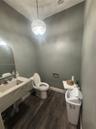 Floating vanity with integrated basin, stone-finish countertop, arched wall mirror, dark wood-finish flooring, and decorative crystal pendant lighting