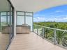 Covered balcony featuring wood-finish flooring, stainless steel outdoor kitchen cabinetry, built-in grill, glass railing, and floor-to-ceiling sliding