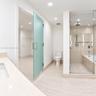 Bathroom featuring stone-finish floor and wall tiles, glass-enclosed shower with integrated tub, frosted glass door, and neutral-toned countertop with
