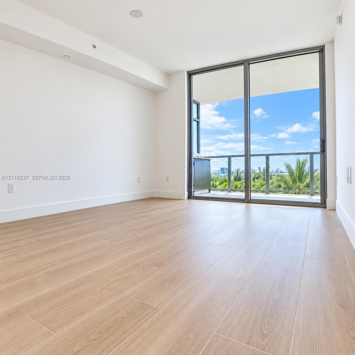 Interior room featuring wood-finish flooring, floor-to-ceiling glass sliding doors, and a private balcony with metal railings