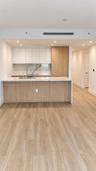 Kitchen featuring flat-panel cabinetry, light-tone wood-finish island, stone-surface countertops, stone-patterned backsplash, and wood-finish flooring