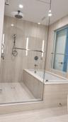 Glass-enclosed wet room featuring a built-in soaking tub, ceiling-mounted rainfall showerhead, handheld shower fixture, and floor-to-ceiling stone-fin