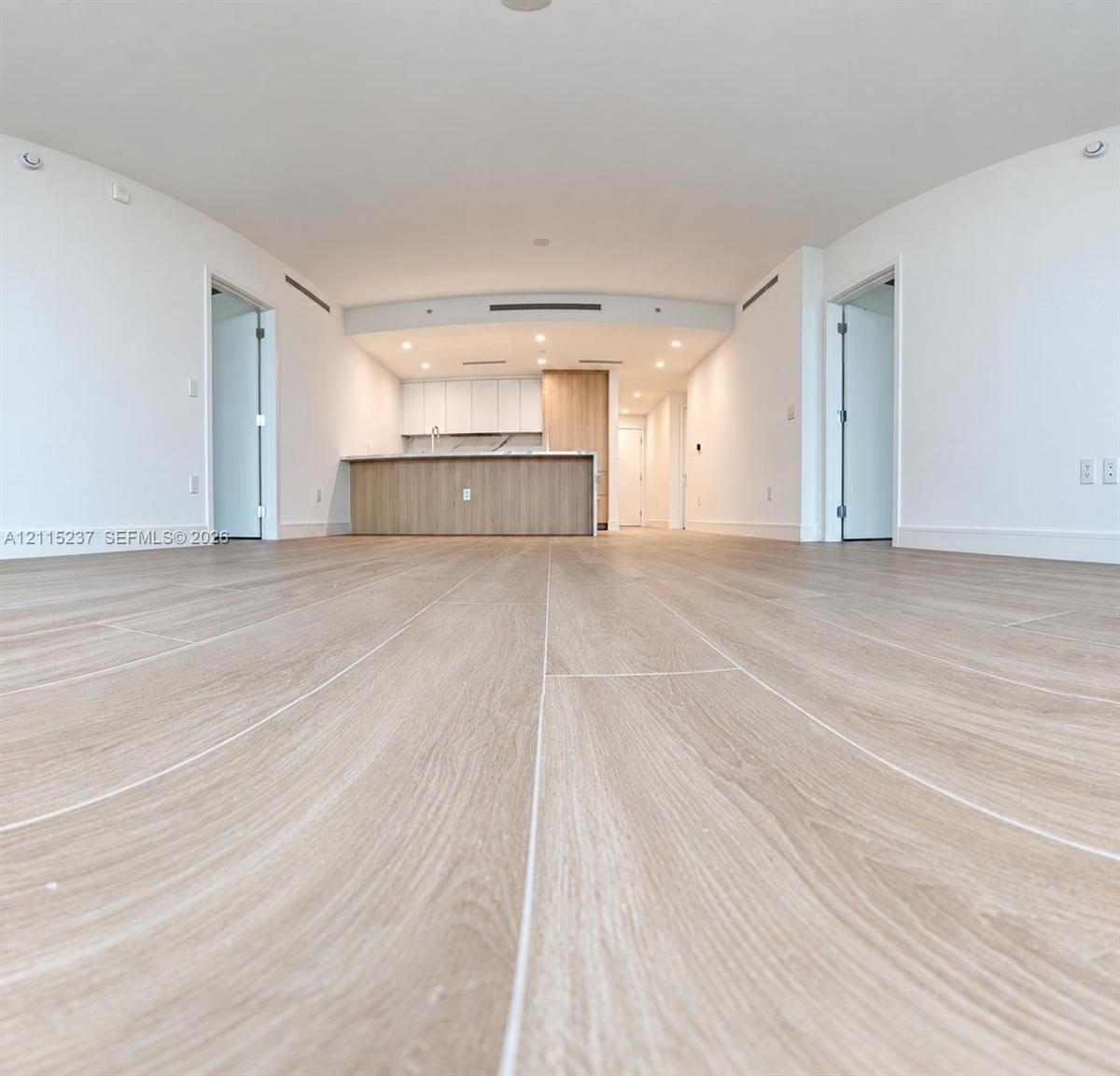 Open-concept interior featuring light wood-finish flooring, recessed lighting, and a kitchen island with stone-finish countertops and wood-grain cabin