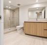 Bathroom featuring a glass-enclosed walk-in shower with tile surround, wood-finish cabinetry, stone-surface countertop, and a wide-format wall mirror