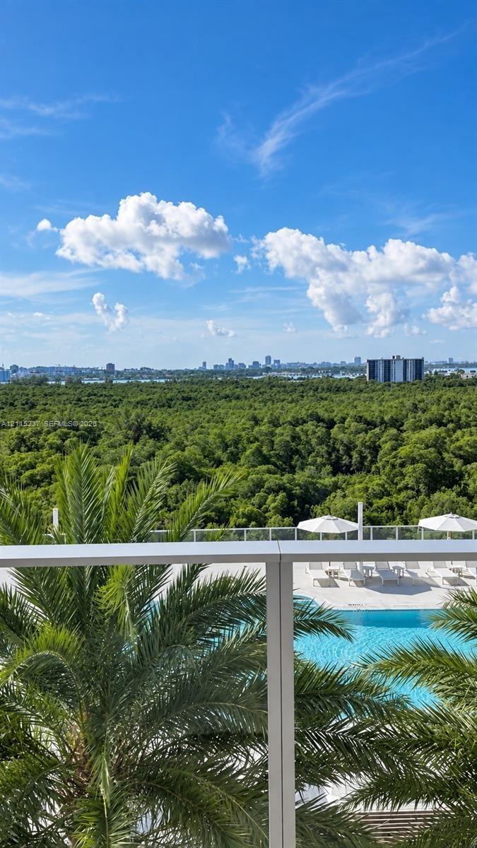 Private balcony with a metal and glass railing, featuring an elevated outlook of a swimming pool, palm trees, and dense forest canopy