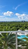 Private balcony with a metal and glass railing, featuring an elevated outlook of a swimming pool, palm trees, and dense forest canopy