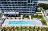 High-rise residential exterior featuring a multi-story glass facade with private balconies, a rectangular swimming pool, integrated landscaping with m