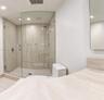 Walk-in shower with a curved glass enclosure and stone-finish wall tile, complemented by a stone-finish vanity countertop and a wall-mounted mirror