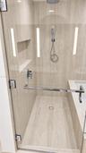 Walk-in shower featuring natural-stone tile surrounds, a rain-style showerhead with a handheld attachment, a built-in recessed niche, and a frameless 