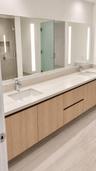 Floating wood-finish vanity with dual integrated rectangular sinks, light-toned stone-finish countertop, integrated linear vertical LED mirror lightin