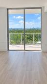 Full-height sliding glass doors with aluminum framing, wood-finish flooring, and a private balcony featuring a glass railing