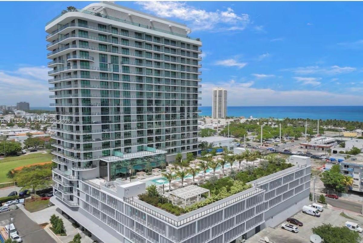 High-rise residential tower featuring a glass-facade exterior, wrap-around balconies, and an elevated terrace level with an outdoor pool, manicured la
