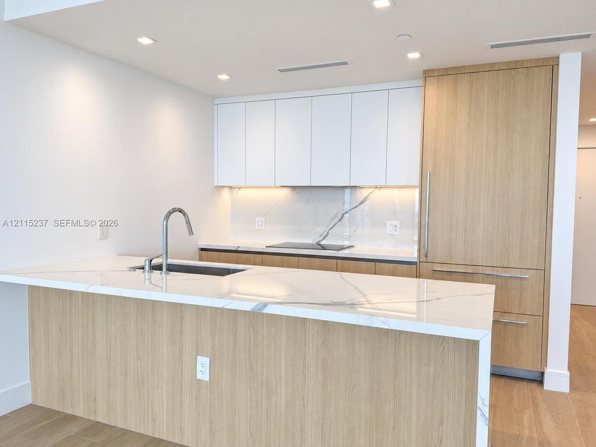 Kitchen featuring a waterfall-edge island with stone-finish countertop, flat-panel cabinetry with wood-finish and matte white cabinetry, integrated re