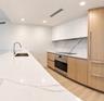 Kitchen featuring an expansive stone countertop with integrated sink, wood-finish cabinetry, white matte upper cabinets, stone backsplash with veining