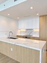 Kitchen featuring a waterfall-edge stone countertop, wood-finish cabinetry, integrated appliances, under-cabinet lighting, and a stone slab backsplash