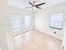 Neutral-toned tile flooring, three windows with adjustable roller shades, and a ceiling-mounted light fixture with a multi-blade fan