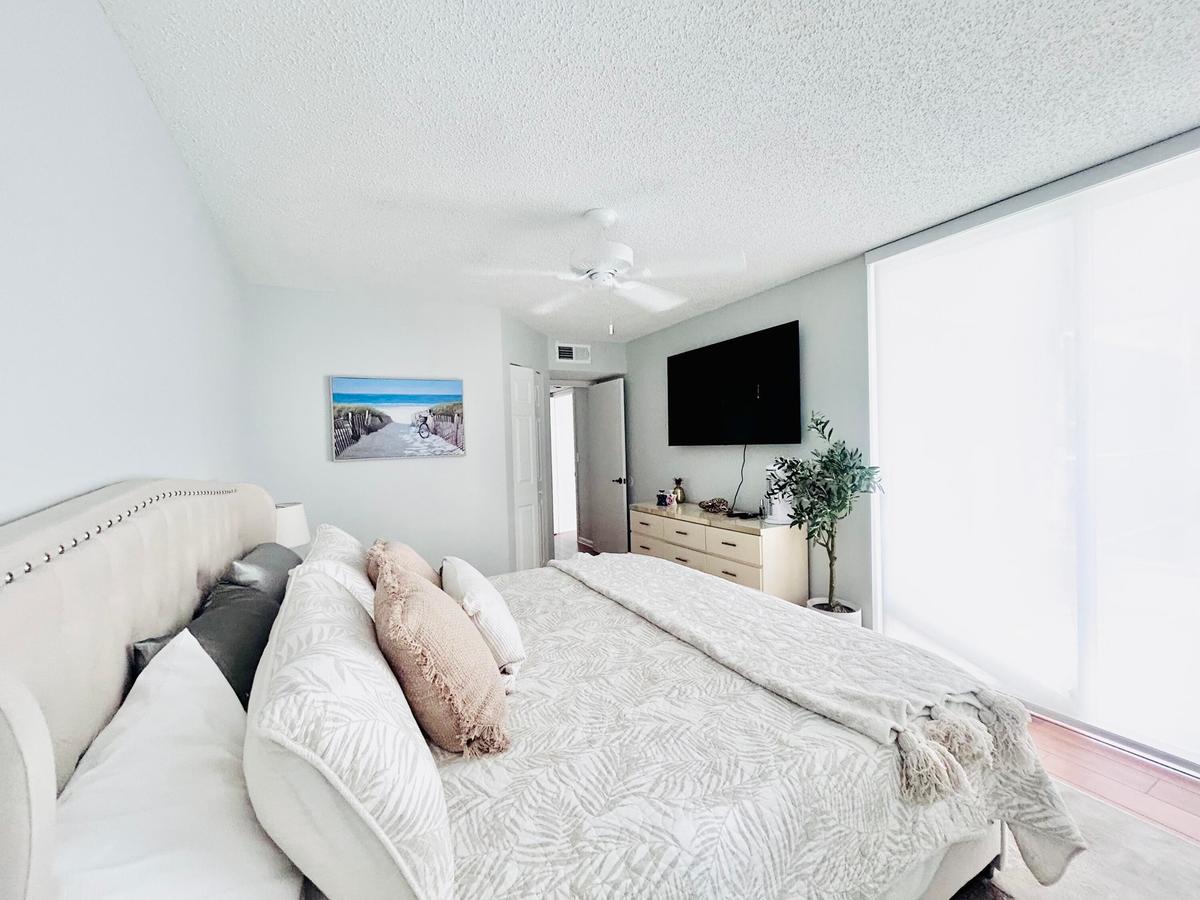 Spacious room with a ceiling fan, light-colored walls, and large windows featuring white roller shades