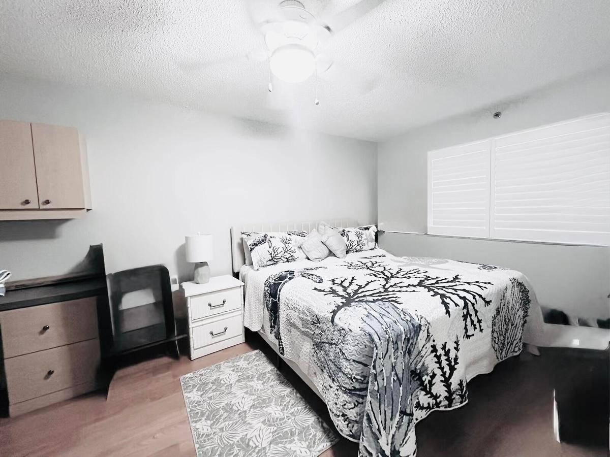 Bedroom featuring wood-finish flooring, a ceiling fan with integrated lighting, and plantation shutters