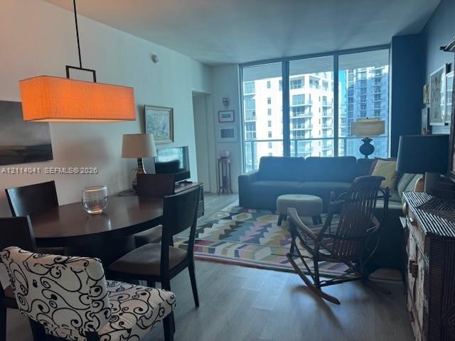 Floor-to-ceiling windows, wood-finish flooring, and a linear pendant light fixture
